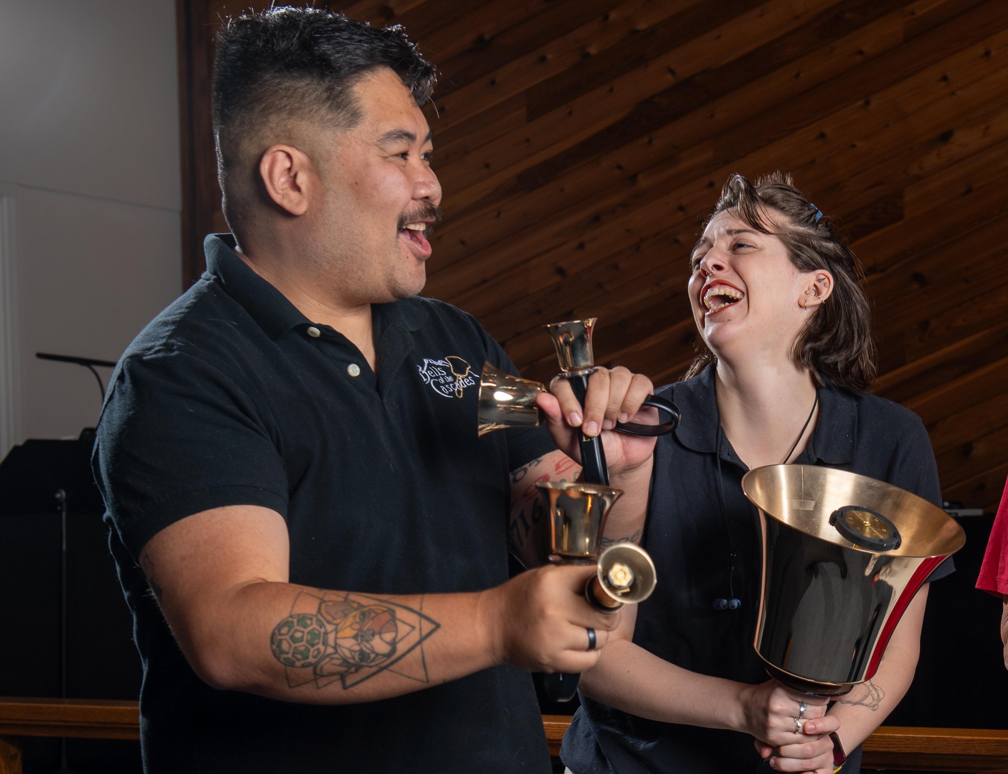 Two handbell musicians smile and laugh while holding their instruments.